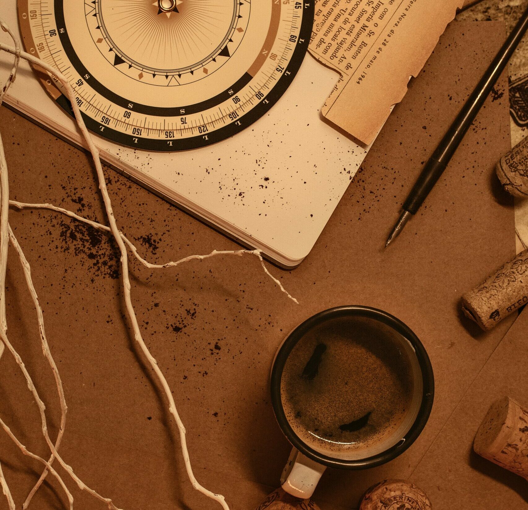 Cup of coffee on brown desk with open notebook, old-style compass, black pen, and corks