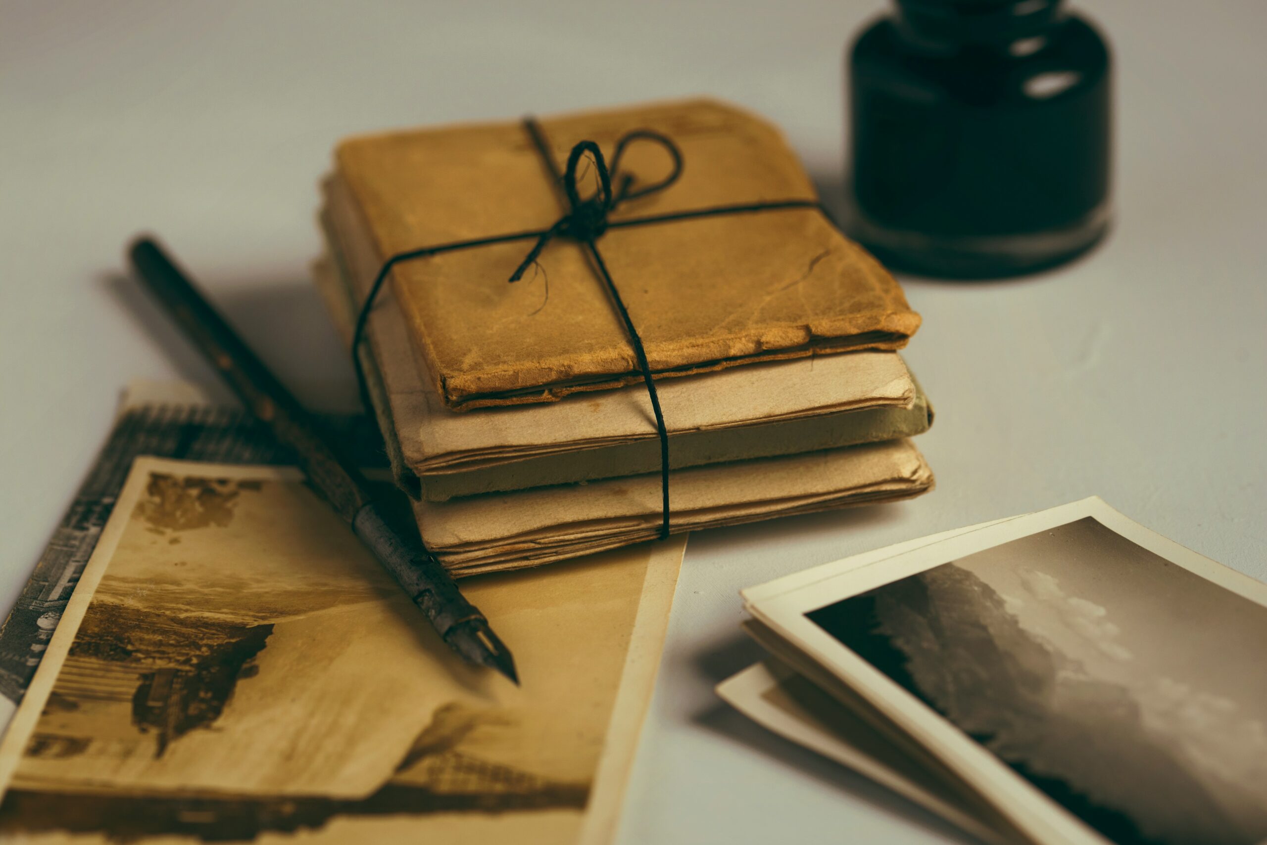 Stack of brown wrapped letters next to photographs, fountain pen, and ink pot.