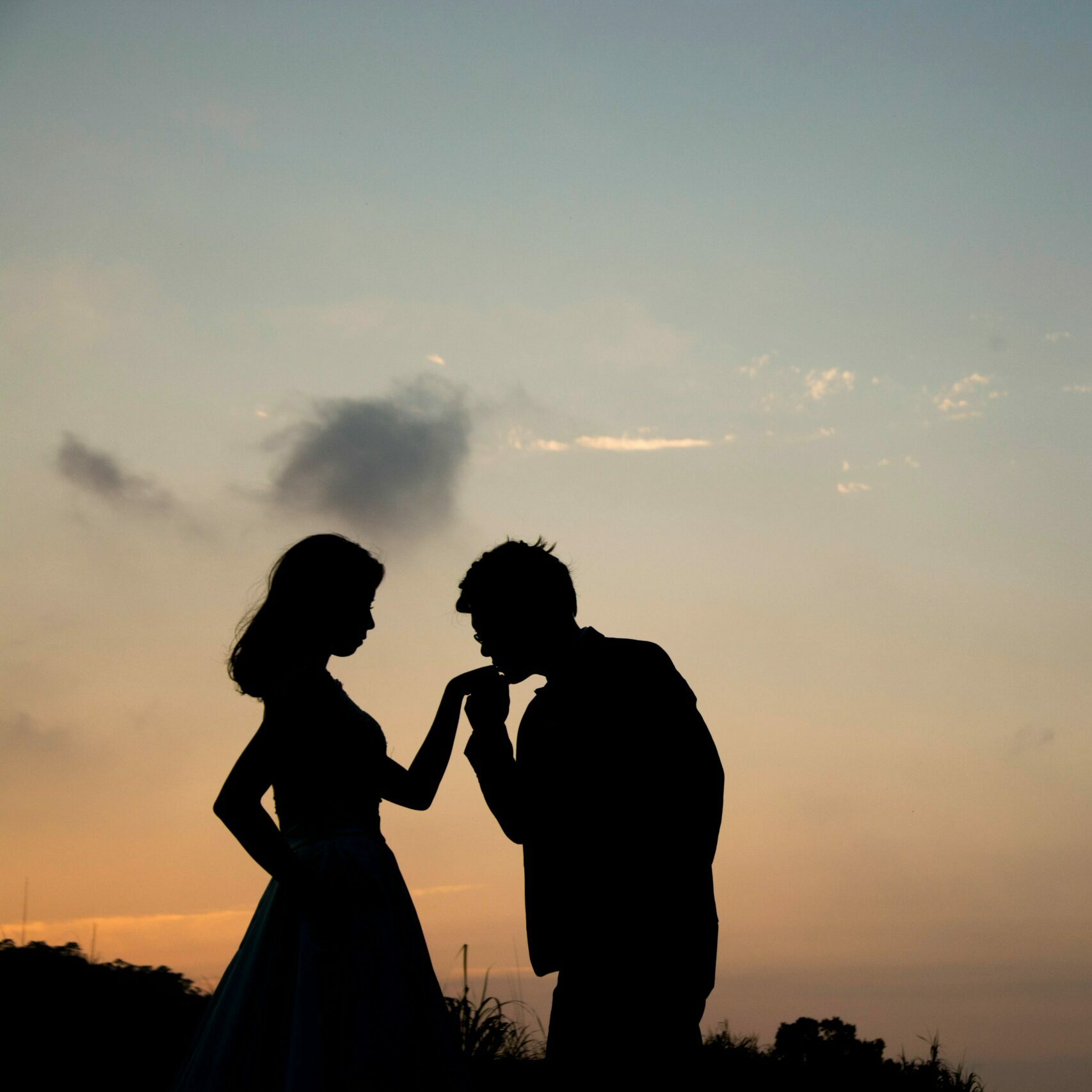 Silhouette of man kissing woman's hand with sunset background