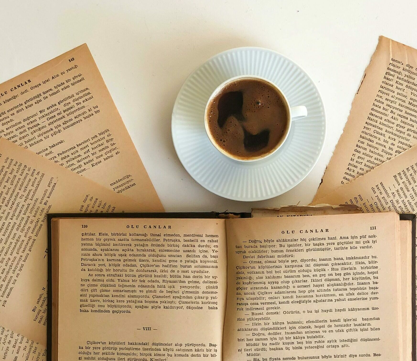 Black coffee in white cup on white plate surrounded by books and book pages