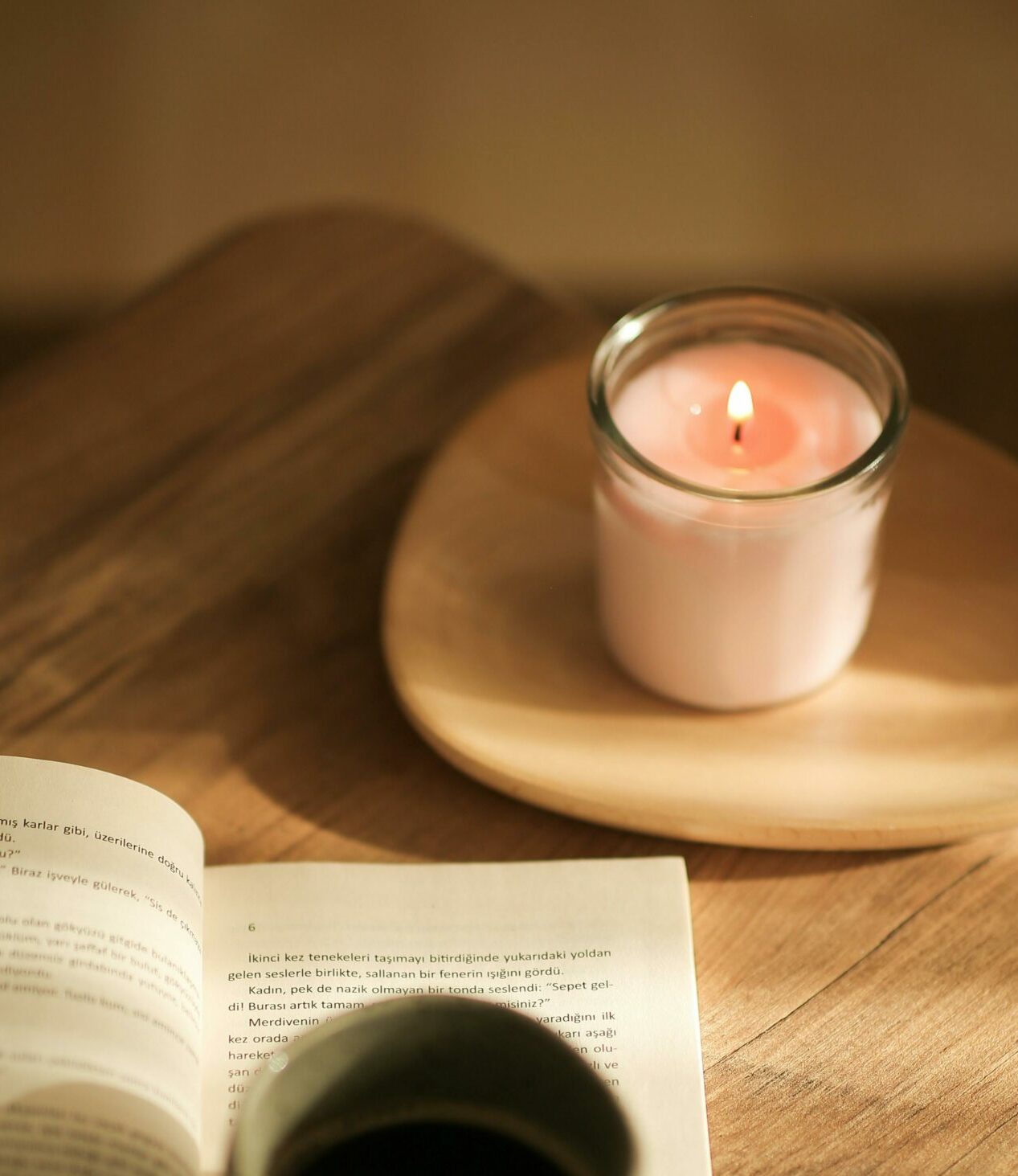 Lit white candle on brown wooden desk near cup of coffee and a book